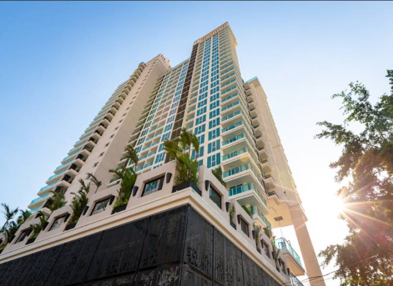 Apartment construction in Pattaya with a tall skyscraper surrounded by palm trees and a blue sky.
