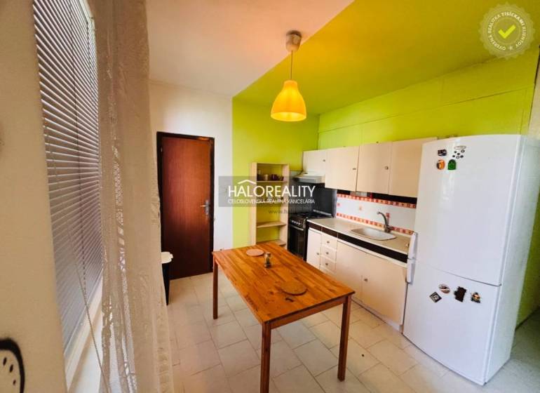 A kitchen in a 3-room apartment with a green wall, a wooden table, and white cabinets.