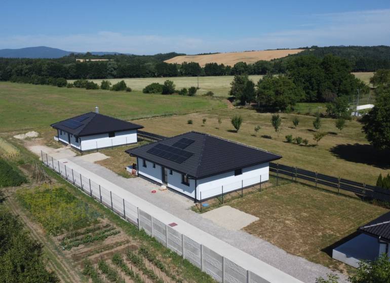 Family houses in Podlužany with modern roofs and solar panels in the field.