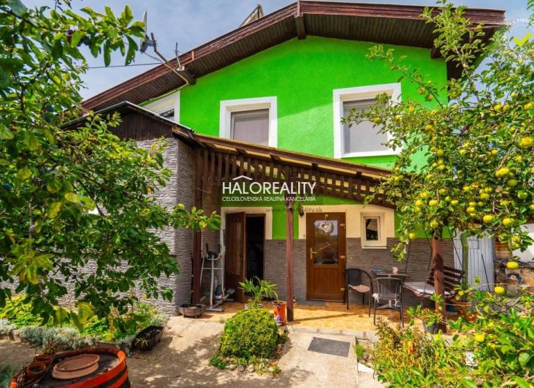 A family house in Banská Štiavnica with a wooden veranda, surrounded by greenery and fruit trees.