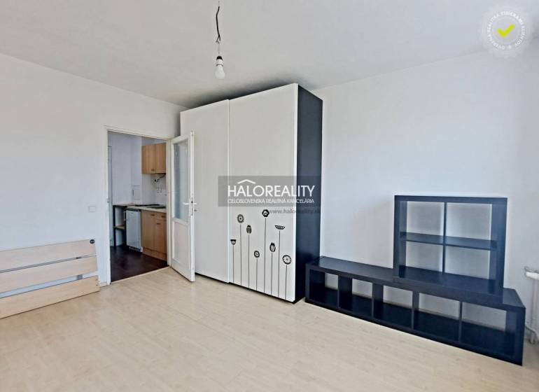 Studio apartment with white furniture, opening into a small kitchen; empty space, bright walls.