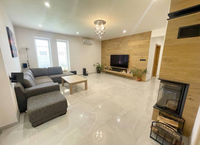 Living room in a family house with a fireplace, corner sofa, and television on a wooden wall.