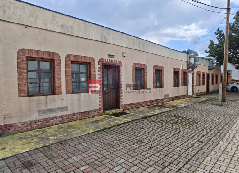 Partizanska Street in Svätý Jur with commercial spaces, brick windows and doors, paved sidewalk.