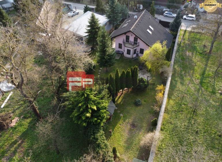 A family house in Píla surrounded by trees with a landscaped garden and neighboring buildings.