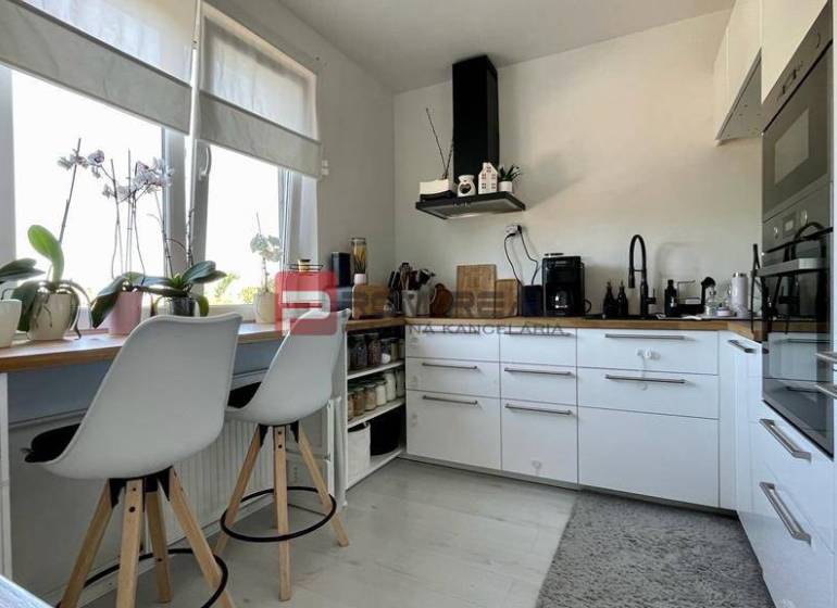 A kitchen in a 3-room apartment with white cabinets and bar stools.