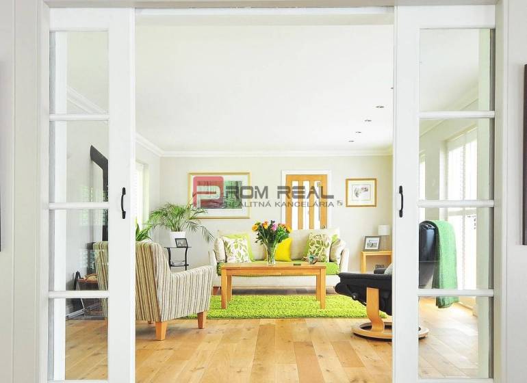 A bright living room with glass doors, wooden flooring, a sofa, and a table in a studio apartment.