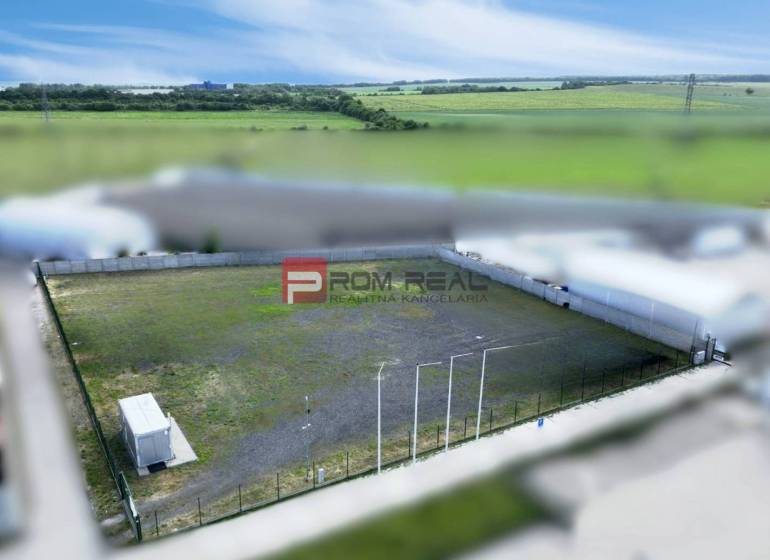Production premises in Pezinok with a fenced outdoor area and a container, surrounded by fields.