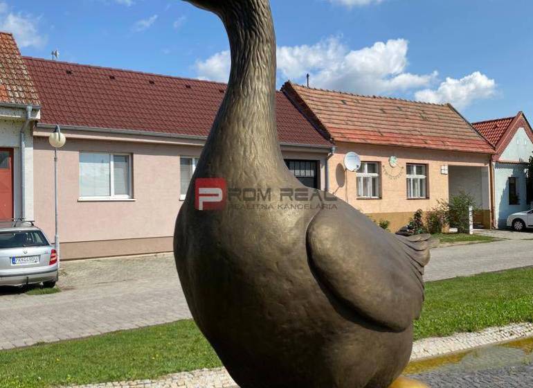 A statue of a goose with a gilded egg on Slovenský Grob street, with warehouses and halls in the background.