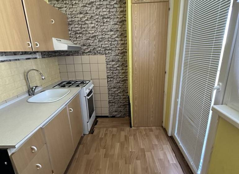 A kitchen with wooden cabinets, a stove, and a sink in a studio apartment.