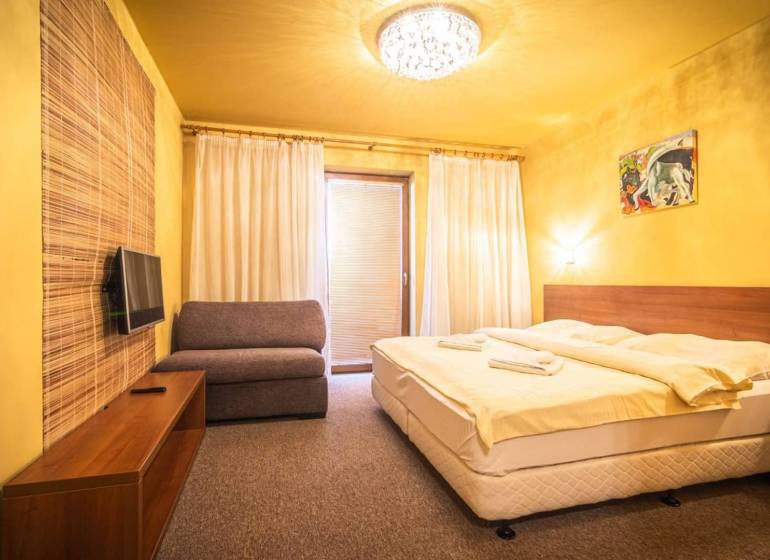 A bedroom in a holiday apartment with a double bed, a sofa, and a television.