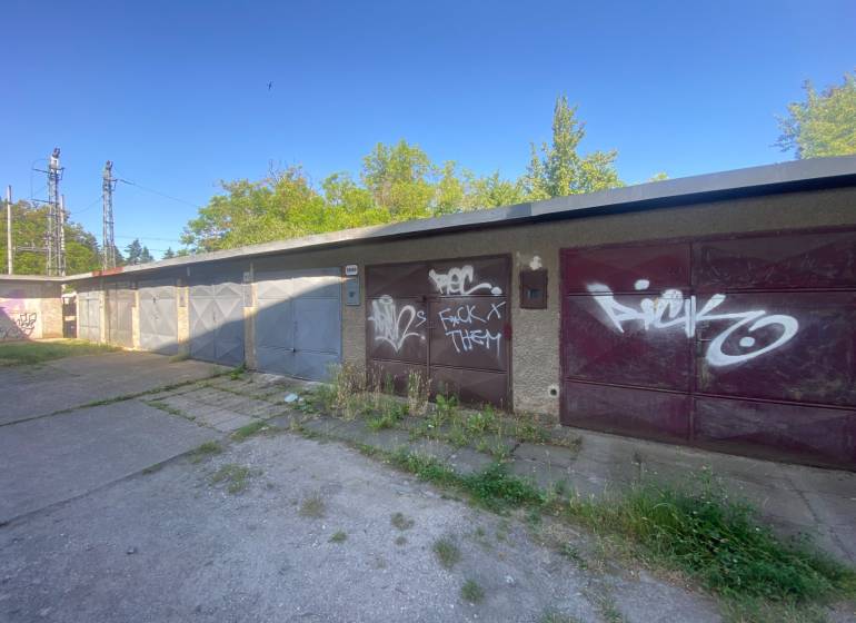 Garages in Zvolen with graffiti on the doors, surrounded by greenery and a concrete area.