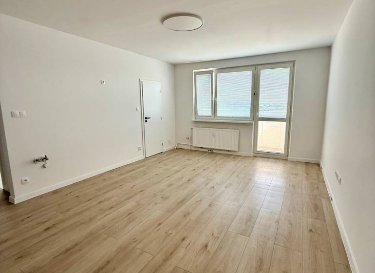 An empty room with a wooden floor and a large window in a two-room apartment.