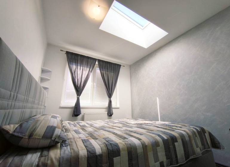 Bright bedroom in a 2-room apartment with a bed, large window, and skylight.