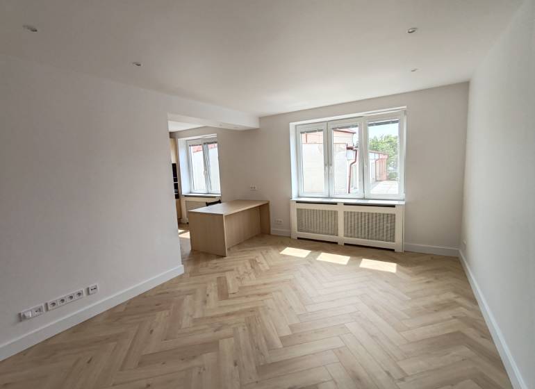 Bright living room in a two-room apartment with wooden flooring and windows.