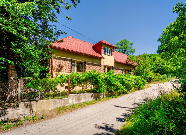 A family house on a quiet street in Púchov with lush greenery and a fence.