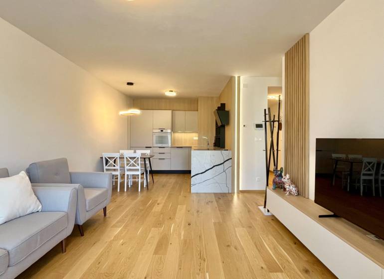 Living room in a two-room apartment with wooden flooring, a sofa, and a television.