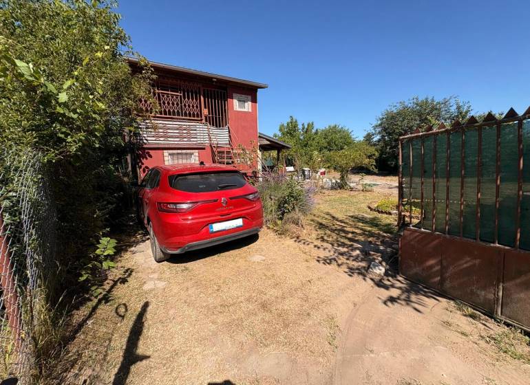 Gardens in Komárno with a red car, a house, and greenery behind the gate.