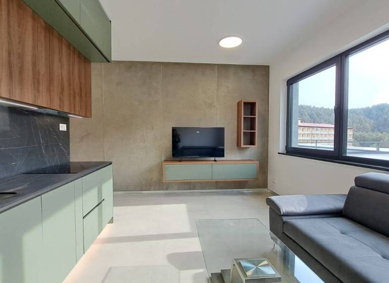A kitchen unit with a TV and a couch in a 2-room apartment with a large window.