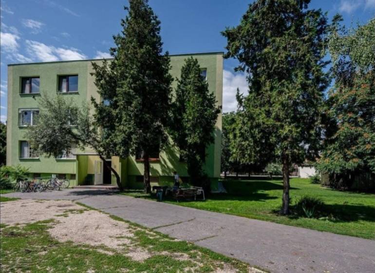 A hut surrounded by trees in Číčov, next to an asphalt road and bicycles.