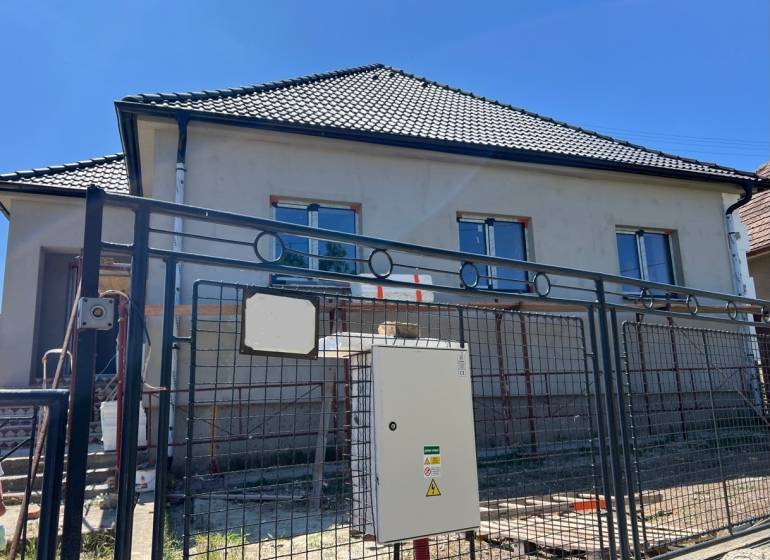 A family house in Sasinkovo on Sasinkovo Street with an unfinished facade behind a metal fence.