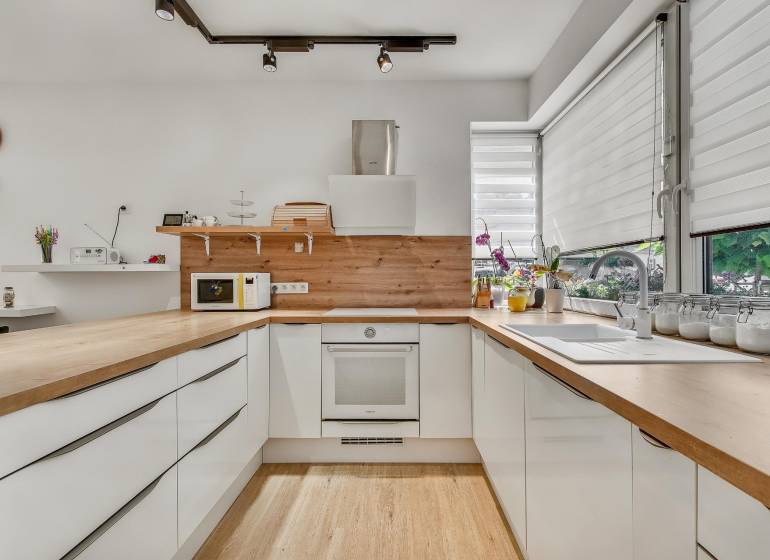 A kitchen in a family house with light cabinets, a wooden countertop, and large windows.