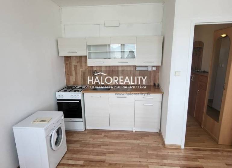 A kitchen in a studio apartment with a stove, dishwasher, and cabinets, wooden floor.