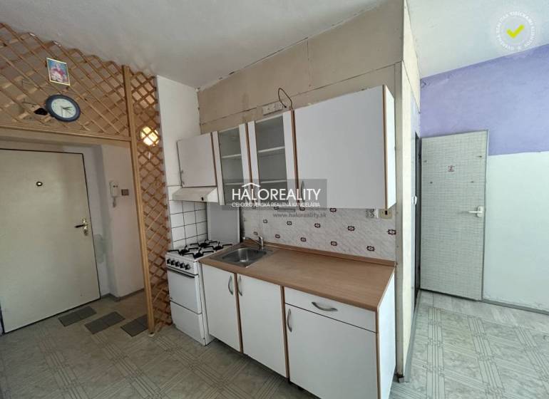 A kitchen in a studio apartment with a gas stove and cabinets, on a white wall.