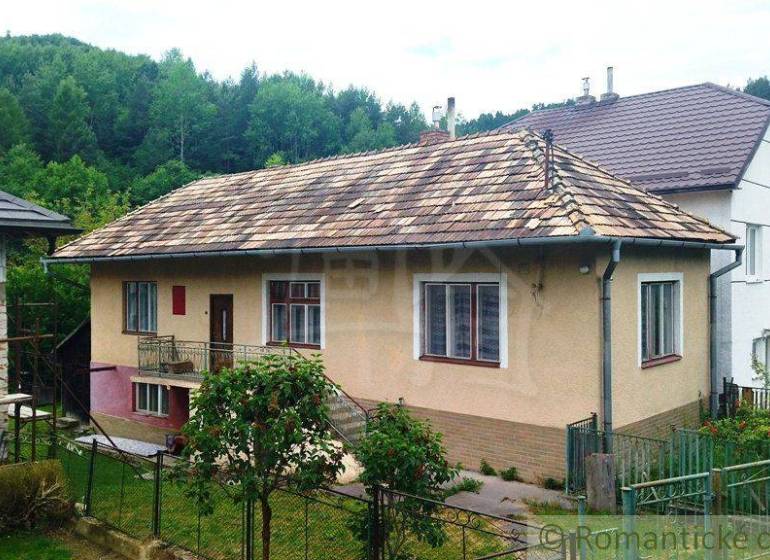 A family house in Fričovce with a sloped roof, garden, and surrounding forest.