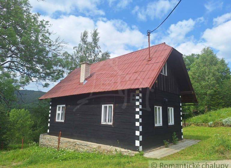A traditional wooden cottage in Klokočov with a red roof, surrounded by greenery and trees.