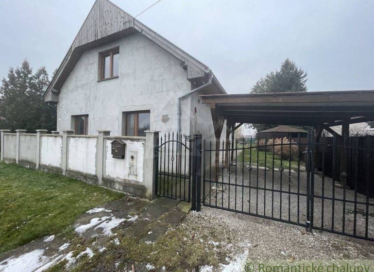 A family house with a white facade and gate, surrounded by a lawn and fencing.
