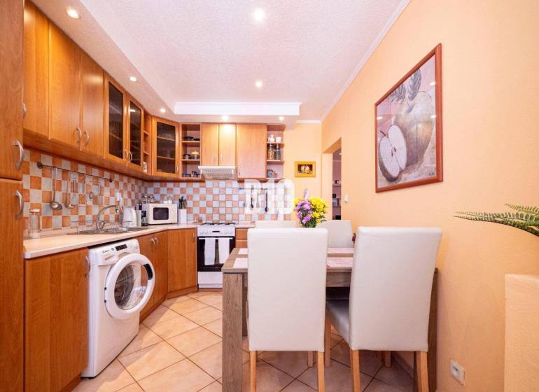 A kitchen in a 3-room apartment with wooden cabinets, a dining table, and a washing machine.