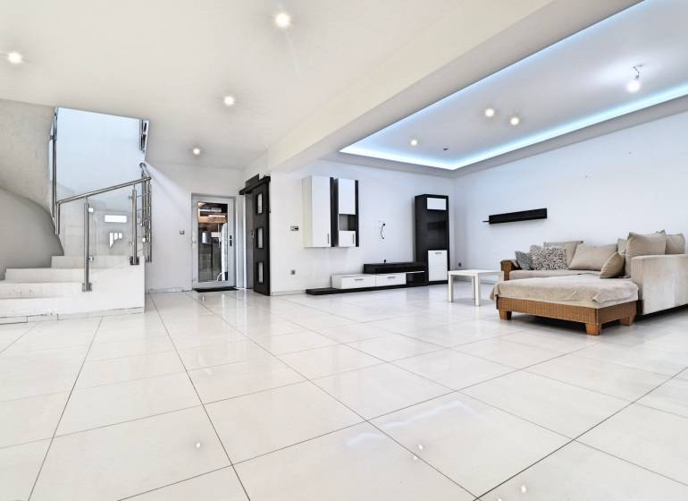 Living room with a sofa and staircase in a family house, light tiles, light walls.