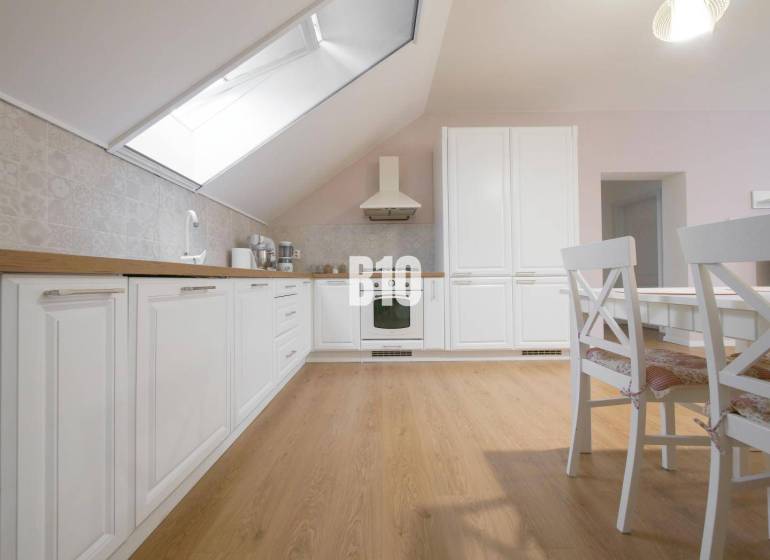 A bright kitchen in a 3-room apartment with white cabinets, wooden flooring, and a dining table.