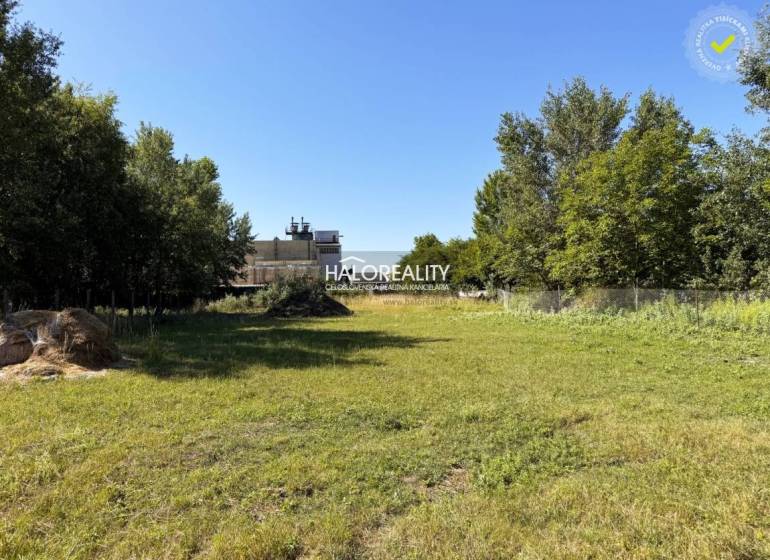 A green plot designated for residential living in Veľký Meder, surrounded by trees and grass.