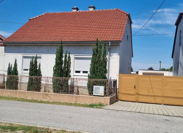 A family house on Riadok in Malacky with a red roof, a front garden, and a wooden gate.