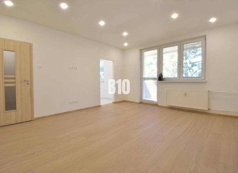 A bright room in a 3-room apartment with wooden flooring and a large window.