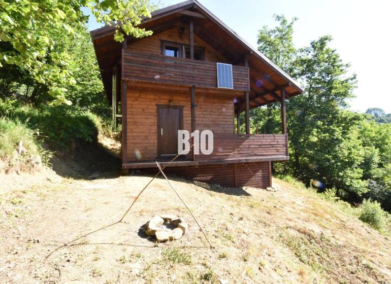 A wooden cabin in nature near Bytča, surrounded by trees and a fire pit.