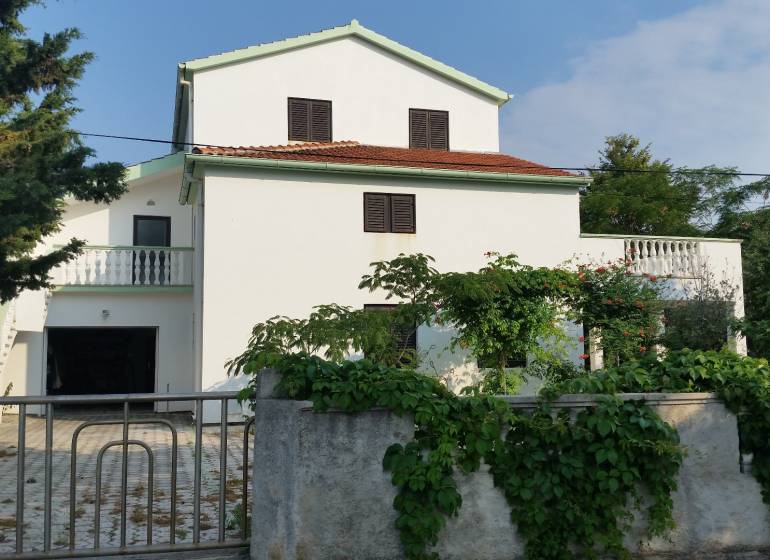 A family house in Vrsi with a white facade and a terrace surrounded by greenery.
