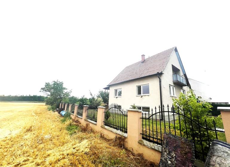 A family house in Veľké Chlievany near a field with a fence and a garden in the background.