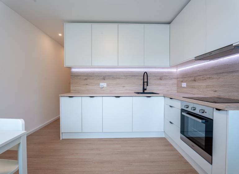 A modern kitchen in a 3-room apartment with white cabinets and a black faucet.