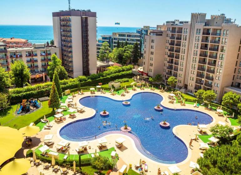A holiday apartment on the Sunny Beach with a pool surrounded by modern buildings and a sea view.