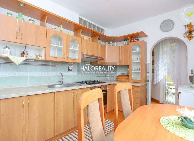 A kitchen in a 3-room apartment with a wooden cabinet, a dining table, and access to the balcony.