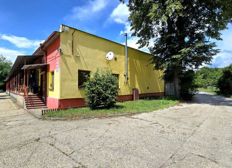 A yellow building with metal stairs, next to it trees, surrounded by greenery in warehouses and halls.