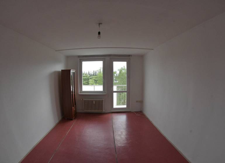 A room with a red floor and a wardrobe in a 2-room apartment, view of greenery.