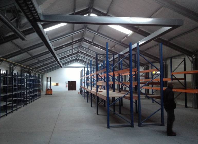 There are empty shelves in the warehouse and a person is standing by them.