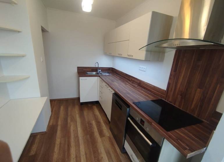 A kitchen unit with a wooden countertop in a 3-room apartment, white cabinets, and built-in appliances.