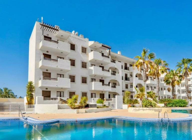 Recreational apartment in Los Alcázares with a pool, palm trees, and blue sky.