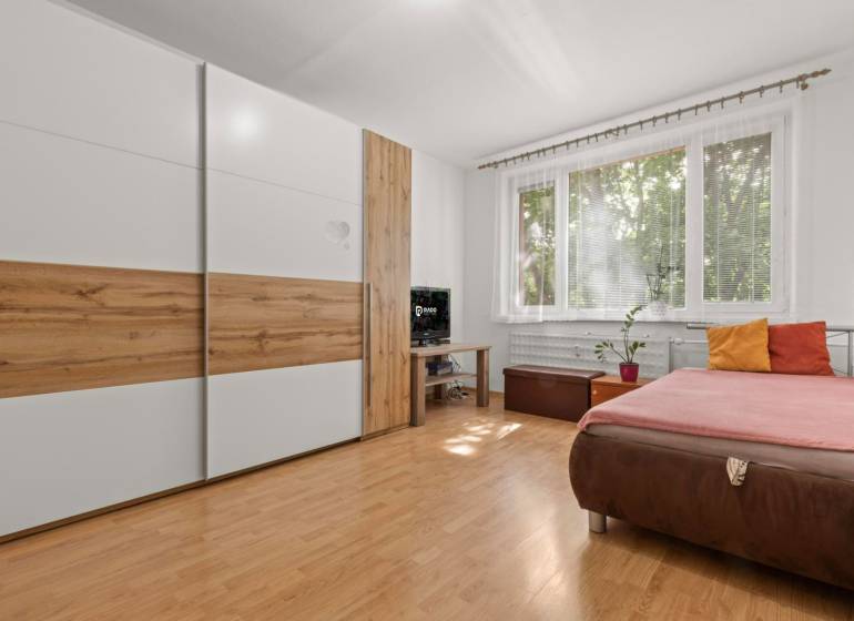 A bedroom with a built-in wardrobe, a sofa, and a window in a three-room apartment.