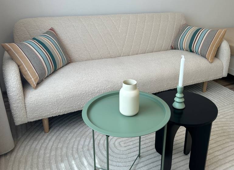 A white sofa with striped cushions, a green and black table in a studio apartment.