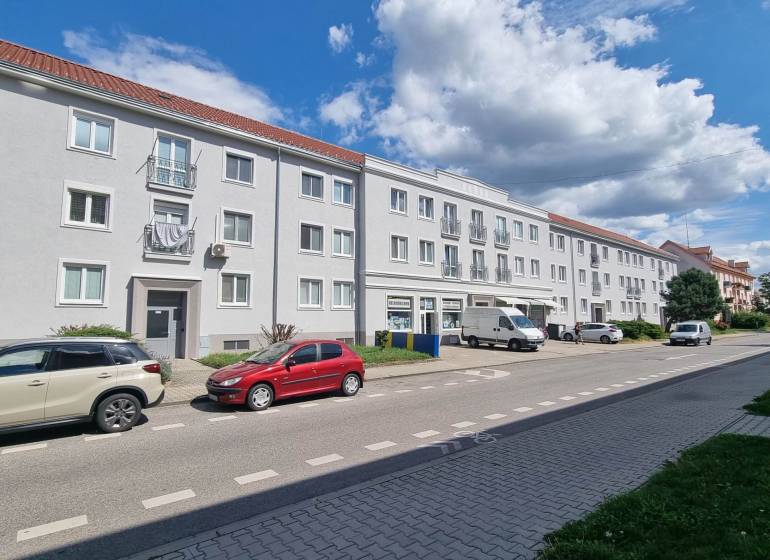 1st May Street in Malacky with parking in front of three-story buildings, visible cars and sidewalk.